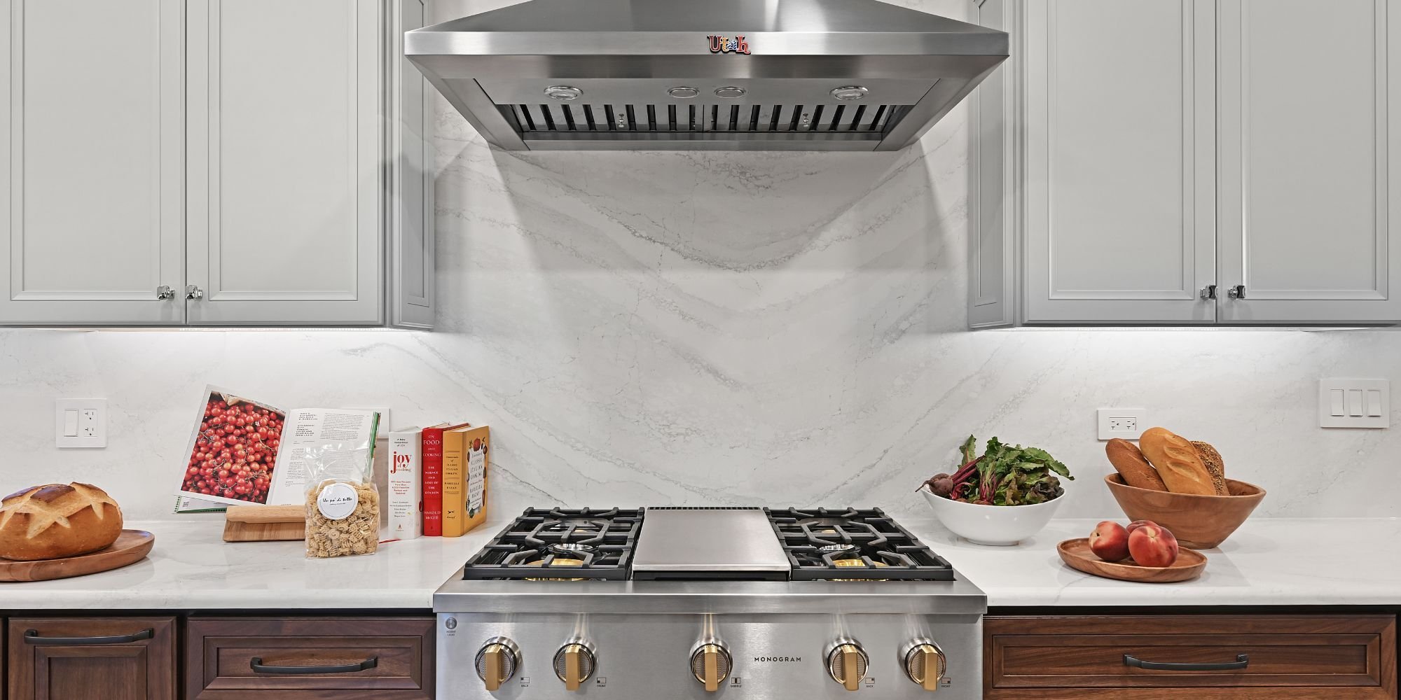 New Monogram gas cooktop and Avallon hood vent surrounded by white Cabria quartz countertops and backsplash in an Aurora, IL kitchen remodel by J&J Con