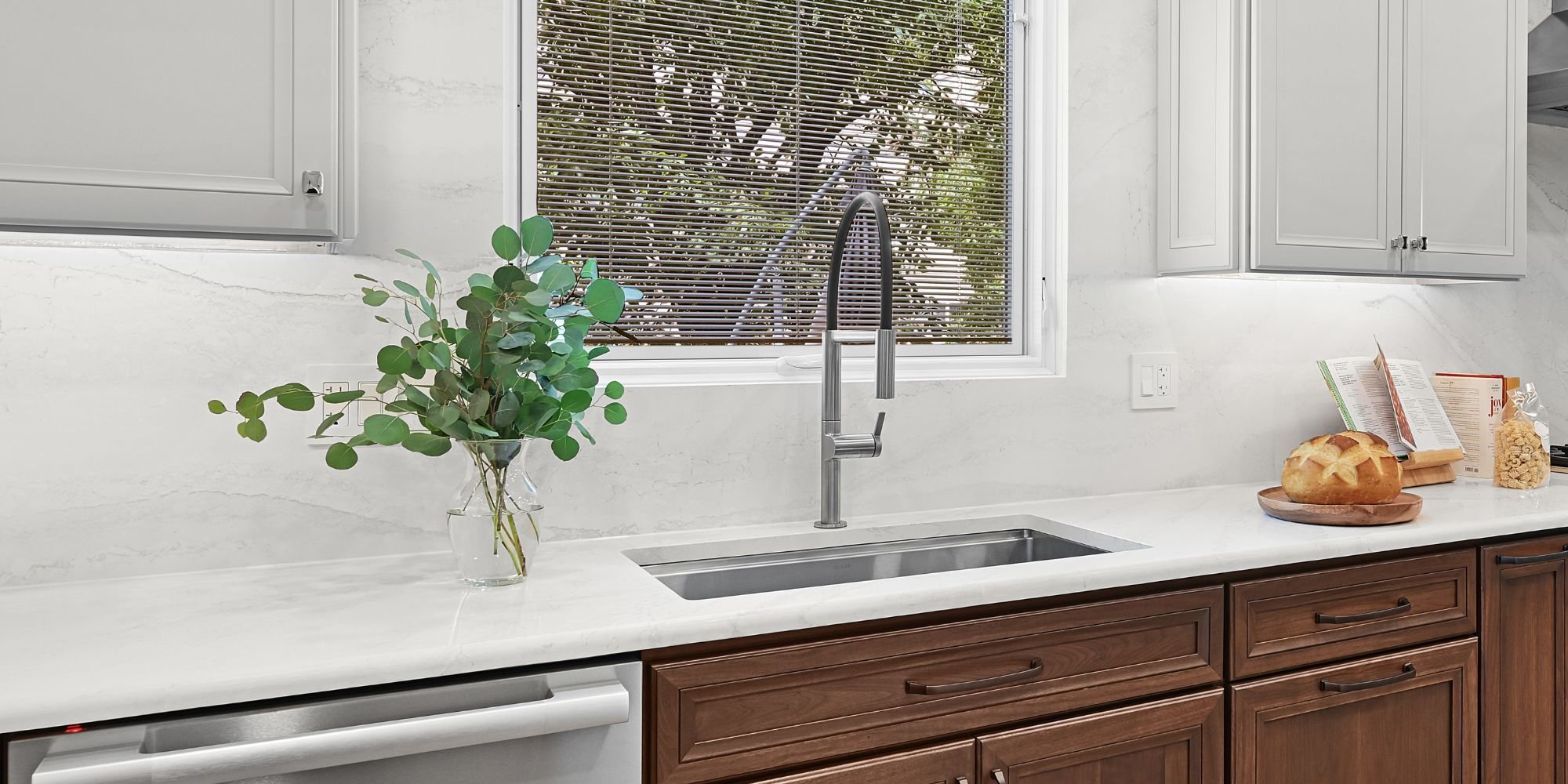 New sink and faucet with a window above, surrounded by white Cabria quartz countertops and backsplash in an Aurora, IL kitchen remodel by J&J Construct