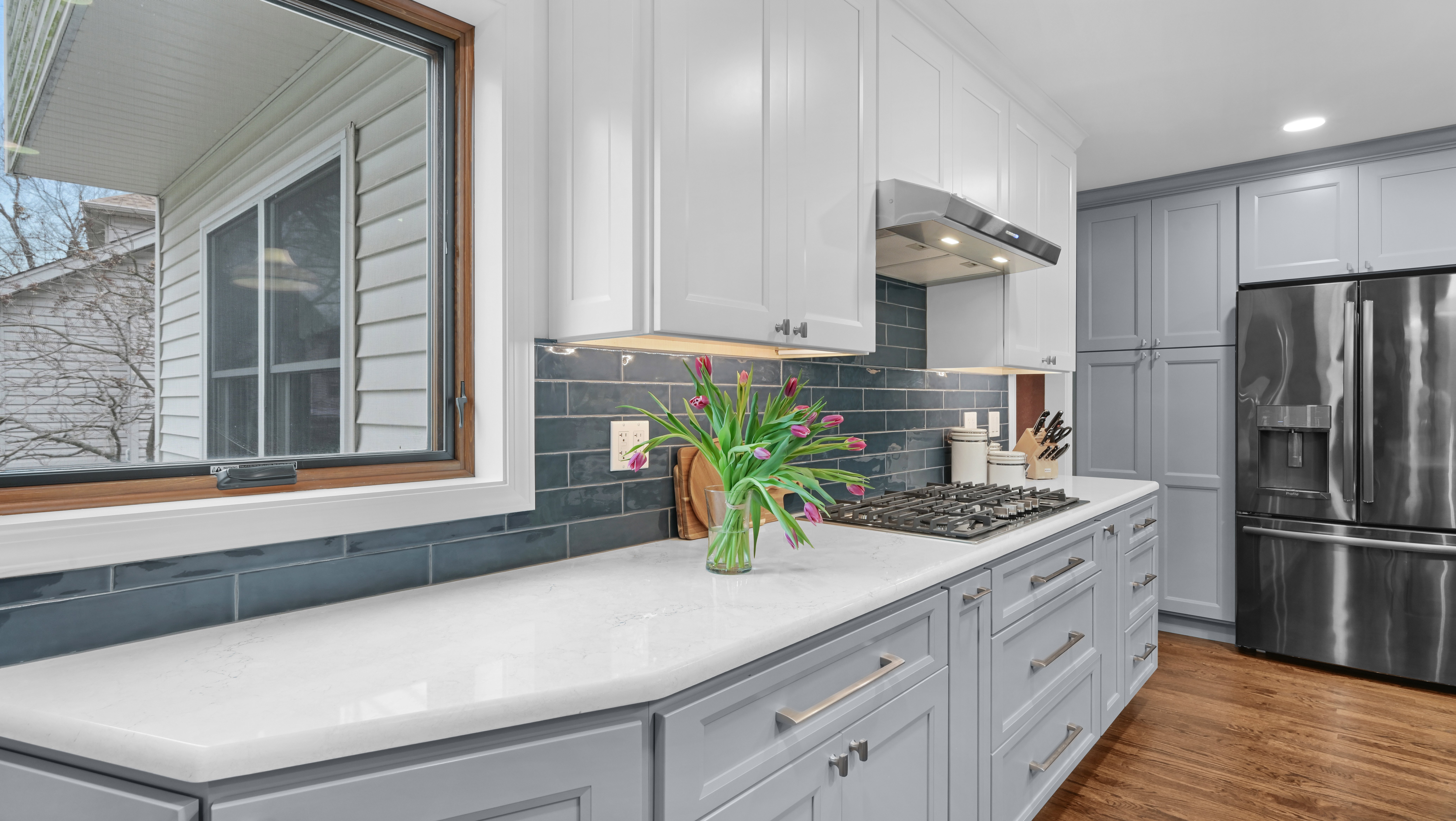 A kitchen remodel featuring white countertops, white and gray cabinets, and a dark tile backsplash in Naperville, IL.
