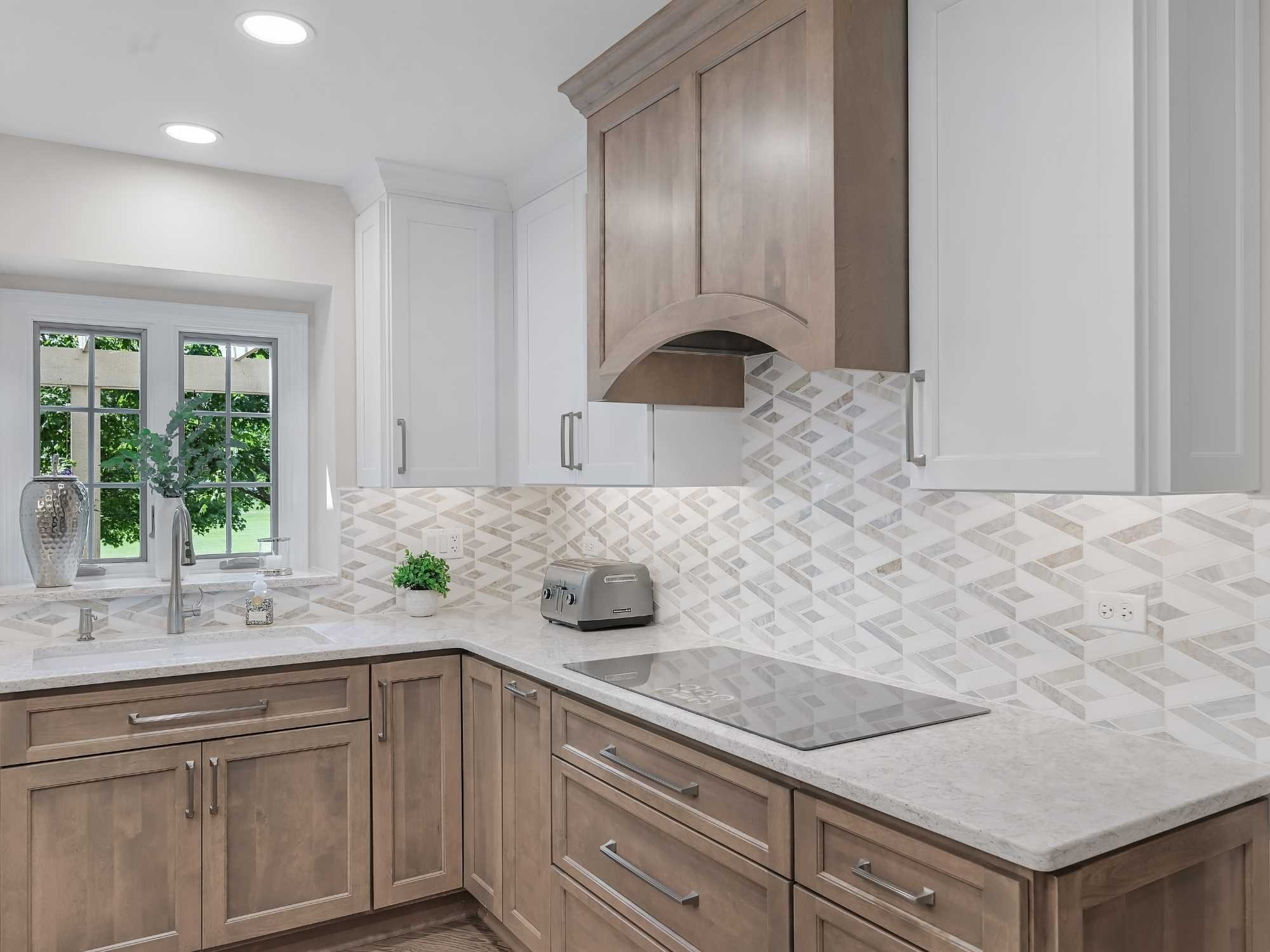 Image of kitchen remodel in Naperville, IL featuring cooktop, custom hood, white cabinets, and modern tile backsplash by J and J Construction